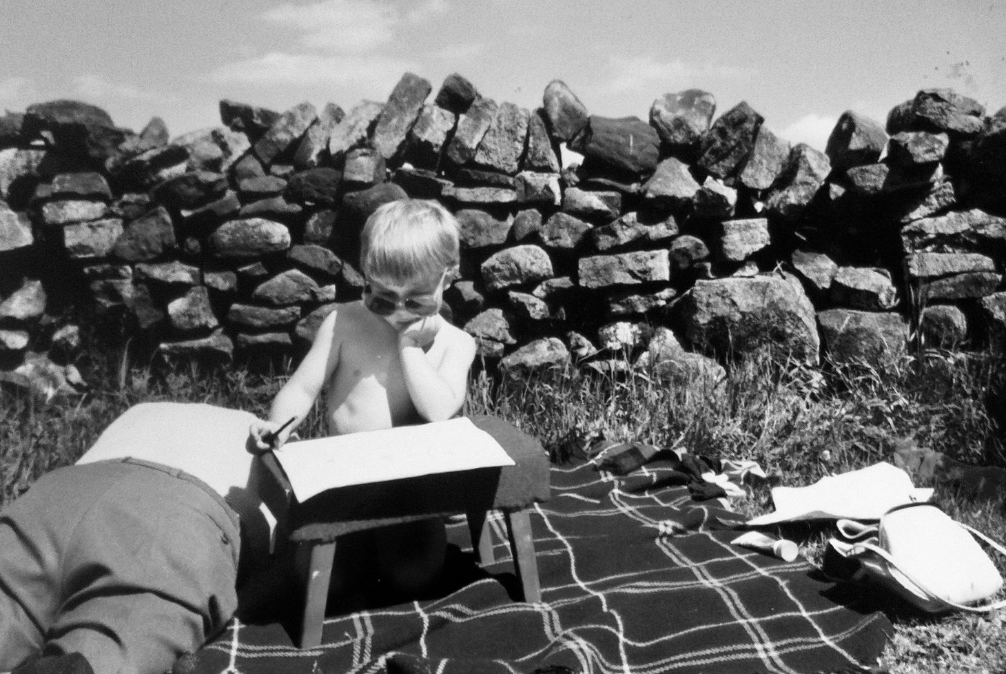 Iain on a picnic blanket as a child in the 80s, writing on a stool while his grandad snoozes